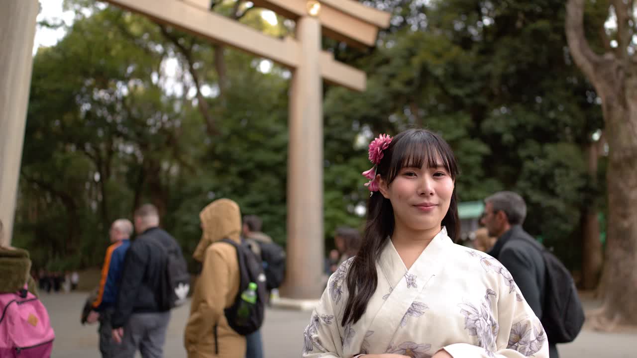 Una donna con un kimono floreale sorride alla telecamera davanti a un grande cancello di legno.