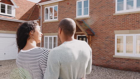 rear view of loving couple standing outside new home on moving day looking at house