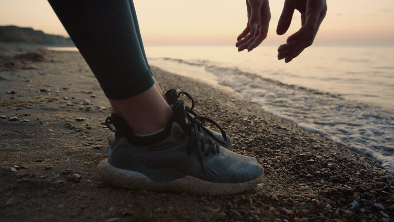 Sportiva sconosciuta che tocca terra con le mani, in piedi sulla sabbia in primo piano.