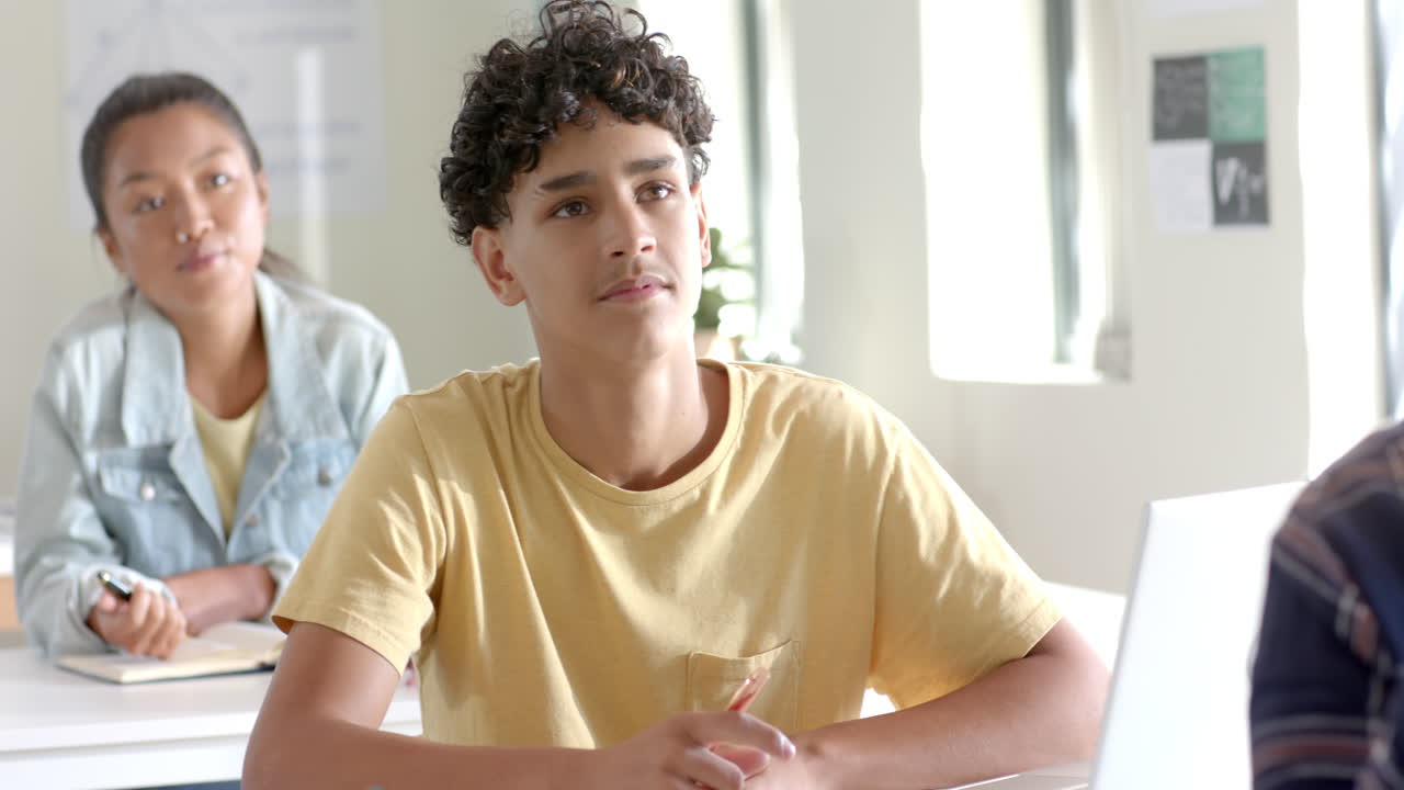 In high school, teenage boy attentively listening and taking notes in classroom