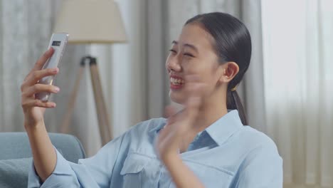 close up of asian woman waving hand having a video call on smartphone while lying on sofa in the living room