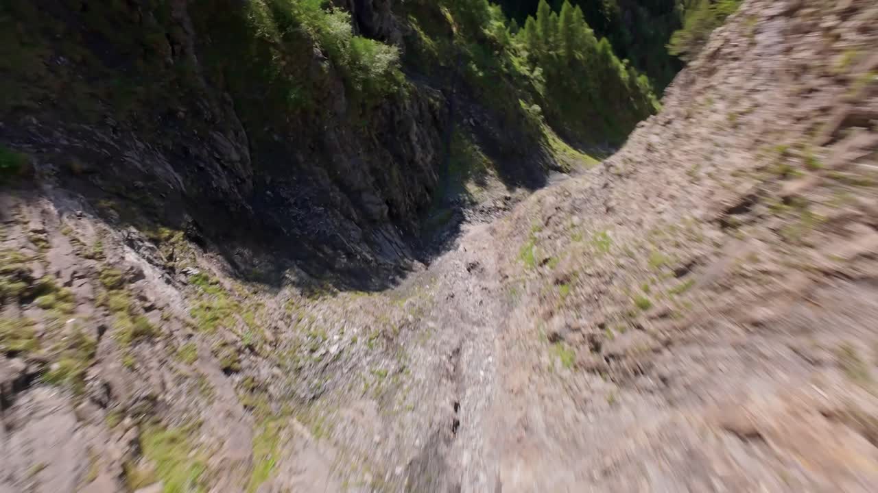 FPV downhill flight along rocky swiss mountains during sunny day in Switzerland. Green forest trees and city in valley.