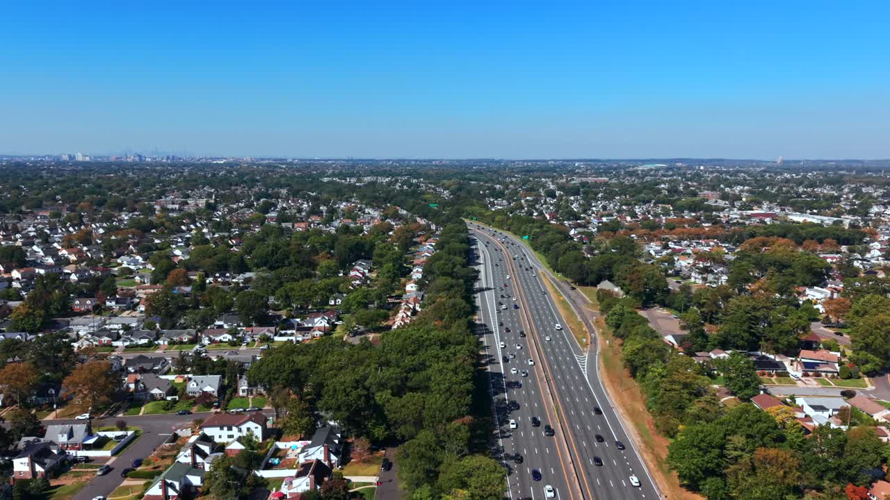 Aerial view of the Southern State Parkway on Long Island, NY during a bright and sunny day with some automobile traffic. The camera dolly in and boom down over the green trees beside the parkway