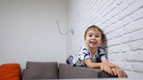 lovely cheerful toddler boy jumps and lies on the sofa. happy boy having fun at home.