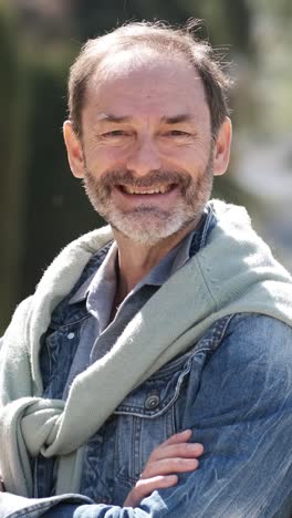 smiling mature man crossing arms in city park. vertical footage