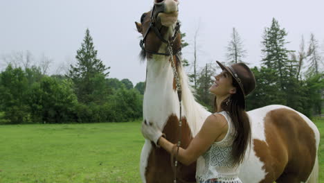 Una-Joven-Vaquera-Entrenada-Frota-El-Cuello-De-Su-Caballo-Pinto,-Riéndose-Del-Evidente-Disfrute-Del-Caballo