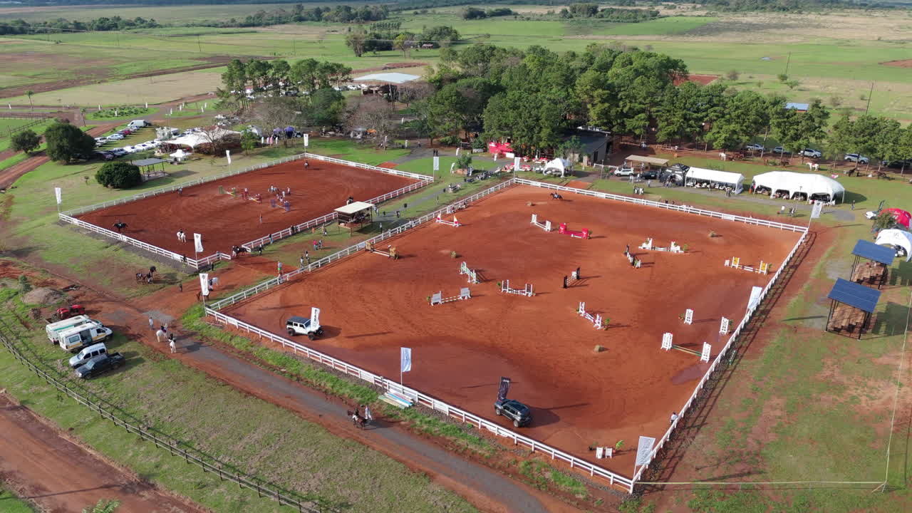 Drone shot of horse and rider jumping an obstacle in sunlit outdoor arena