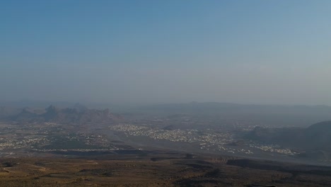 Establecimiento-Y-Reveladora-Toma-De-Una-Piscina-Infinita-Con-Una-Chica-Salpicando-Agua-En-El-Aire-Mientras-Contempla-Una-Vista-Espectacular-De-Las-Montañas-Y-El-Cielo-Azul-En-El-Hotel-Con-Vistas-En-Jebel-Shams-En-Omán