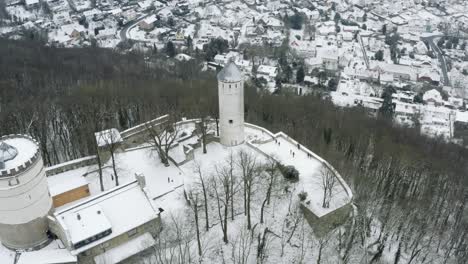 Drone-aerial-of-the-fairy-tale-castle-Plesse-in-winter-with-a-huge-amount-of-snow-on-a-beautiful-mountain-near-Bovenden,-Germany,-Europe