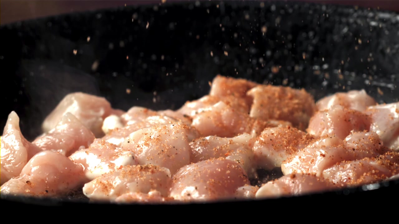 Condimento al rallentatore di pezzi di pollo crudo in una padella