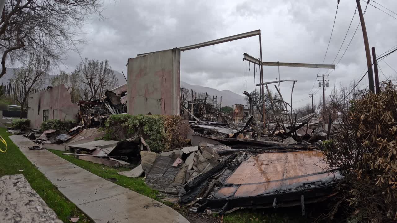 Smoke rises from charred ruins as rain falls over blackened earth. Embers glow, puddles reflect destruction. A powerful scene for news, documentaries, and climate awareness.