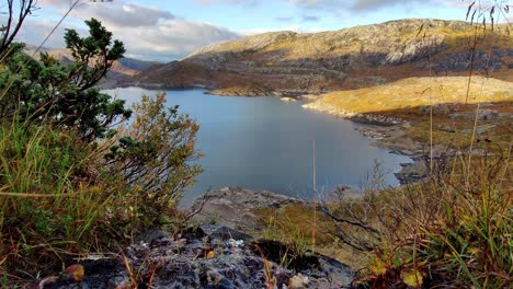 Stream-flowing-gently-into-man-made-dam---Stream-close-to-camera-with-Grondalsvatnet-water-reservoir-for-hydroelectric-powerplant-in-Norway-in-background---Handheld-static-shot-at-sunny-autumn-day