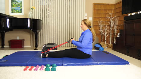 Frau-Sitzt-Auf-Trainingsmatte-Mit-Stretchband,-Fit-Halten,-Zu-Hause,-Statisch