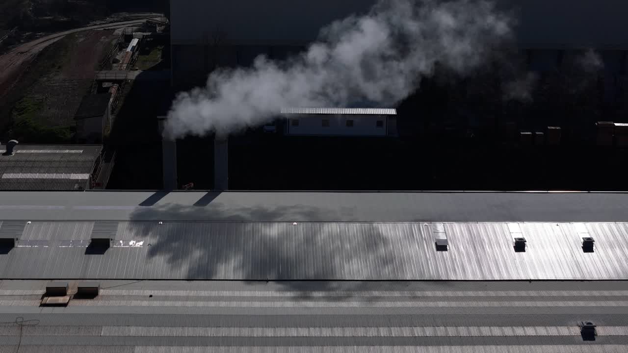 Fabrika çatı yapısının üzerinde yoğun buhar bulutu salan endüstriyel egzoz bacası, üretim faaliyetiyle bağlantılı atmosferik emisyon sürecini ve çevresel etkiyi göstermektedir.