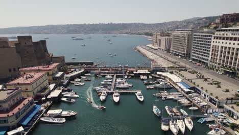 Retroceso-Aéreo-Desde-El-Puerto-De-Vela-De-Nápoles,-Hermoso-Paisaje-Urbano-Costero-En-El-Fondo