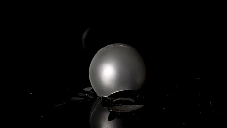 Silver-christmas-ball-drops-on-black-surface-and-shatters