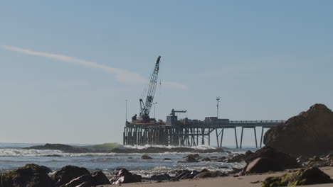 industrial oil rig with crane on pier wharf with ocean waves and rocky beach slow motion 4k 60fps