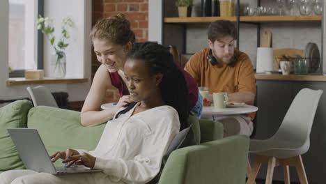 two multiracial female roommates looking something on laptop computer at home