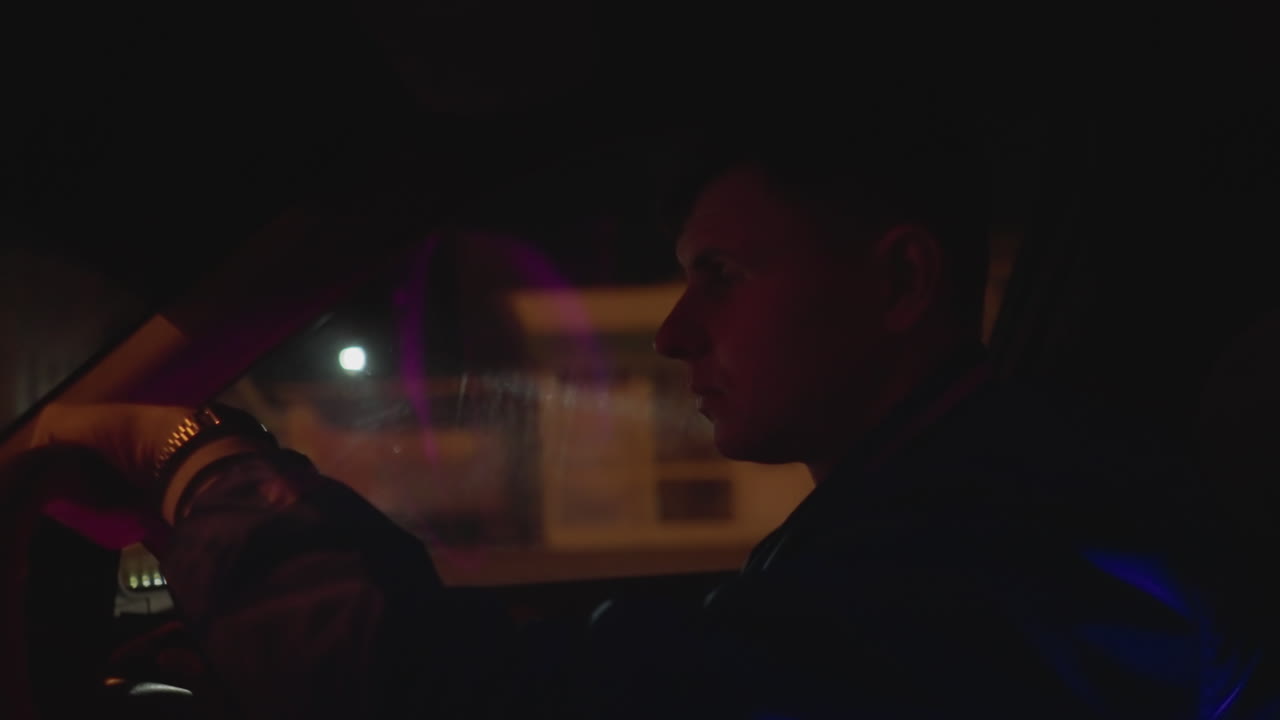 Vigilanza notturna di un autista caucasico per le strade della città. Bokeh al neon e riflessi del traffico, occhiate veloci allo specchietto laterale, mani salde sul volante, ritmo del centro sotto il lampione, ruoli mutevoli