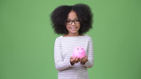 young cute african girl with afro hair holding piggy bank