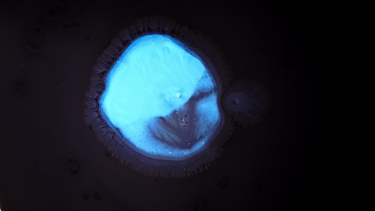 A close-up of substances mixing with vibrant blue liquid in a dark setting