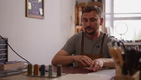 Craftsman-unrolls-natural-leather-sheet-at-table-in-workshop