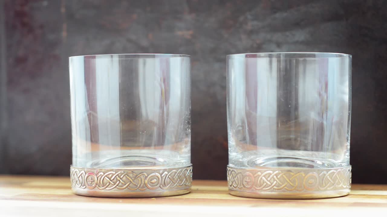 una toma de una mano que vierte una pequeña cantidad de líquido transparente en dos vasos y luego los recoge