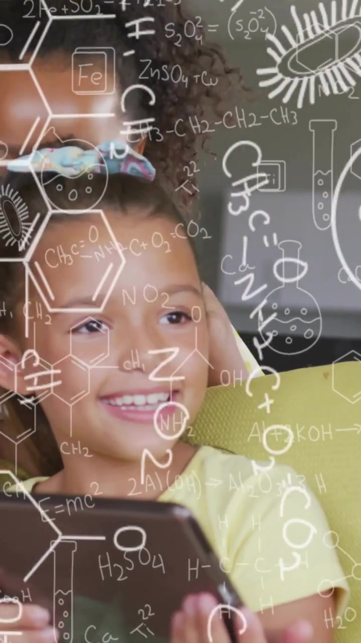 Girls tapping tablet on couch and leaning in, science doodles overlaying screen, causing laughter