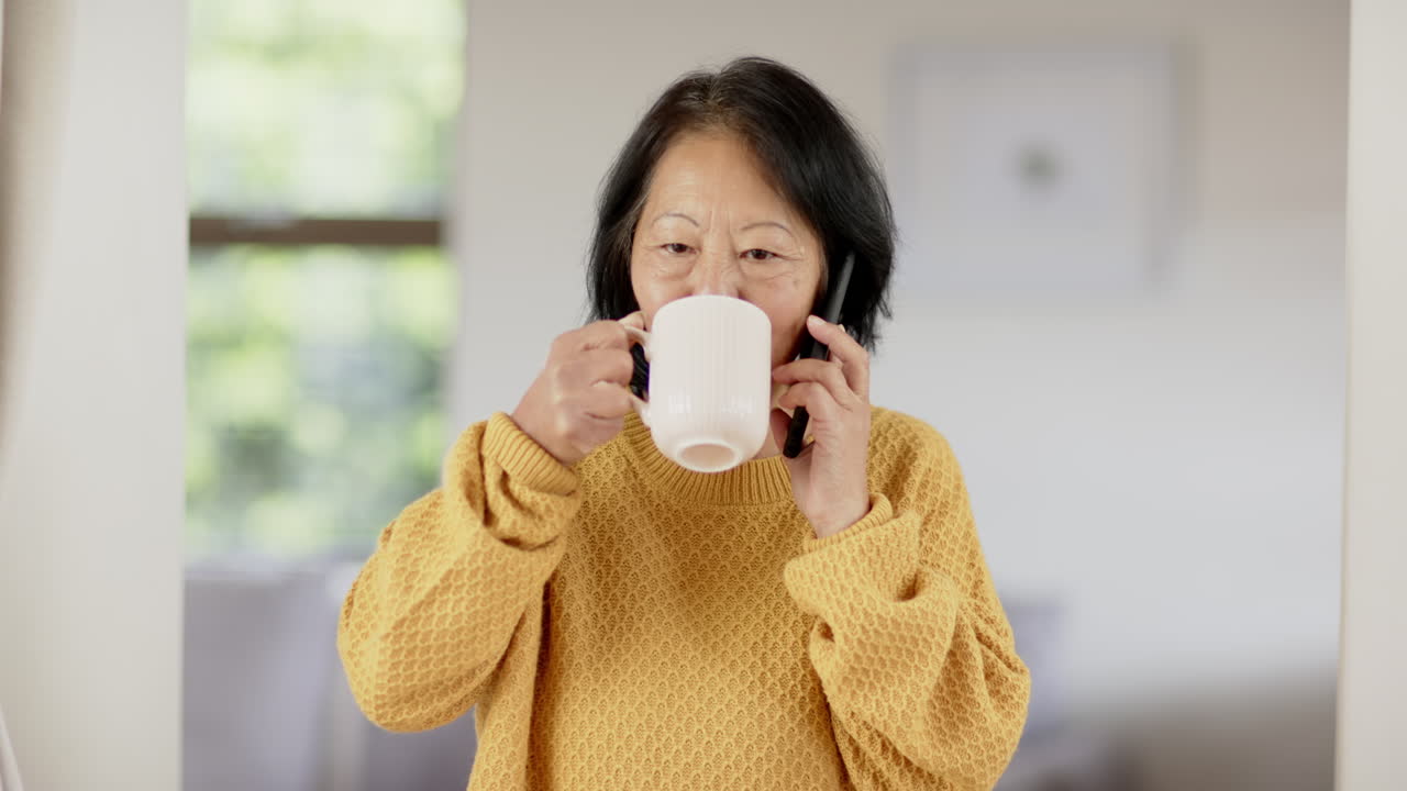 Smiling senior woman talking on phone and holding coffee mug at home