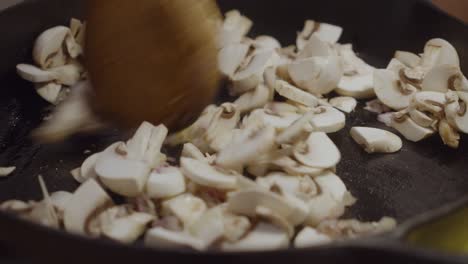 stirring and mixing up white mushrooms with onion slices inside hot frying pan