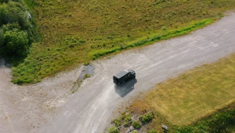 Imágenes-Cinematográficas-De-Cámaras-Aéreas-De-Drones-De-Ritmo-Rápido,-Se-Puede-Ver-Siguiendo-A-Un-Jeep-Negro-Conduciendo-Fuera-De-La-Carretera-A-Gran-Velocidad-Con-Polvo-En-El-Aire-En-Un-Paisaje-Rural-Rodeado-De-Campos-Verdes