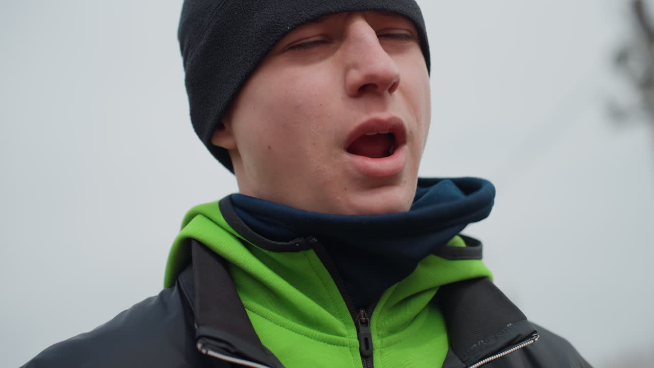 차가운 시선으로 생각에 잠긴 듯한, 부드러운 겨울 조명 아래에서 촬영된 내성적인 남성 인물 사진. 미묘한 감정적 톤과 부드러운 조명을 사용하여 겨울 야외에서 촬영된 사색에 잠긴 남성 이미지