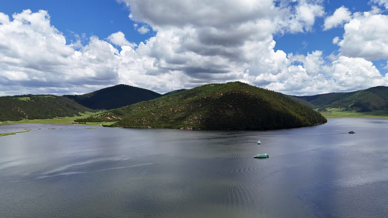 Bukit berhutan menjulang dari danau pegunungan dengan perahu-perahu dan lanskap pegunungan di Taman Nasional Potatso, drone menurun