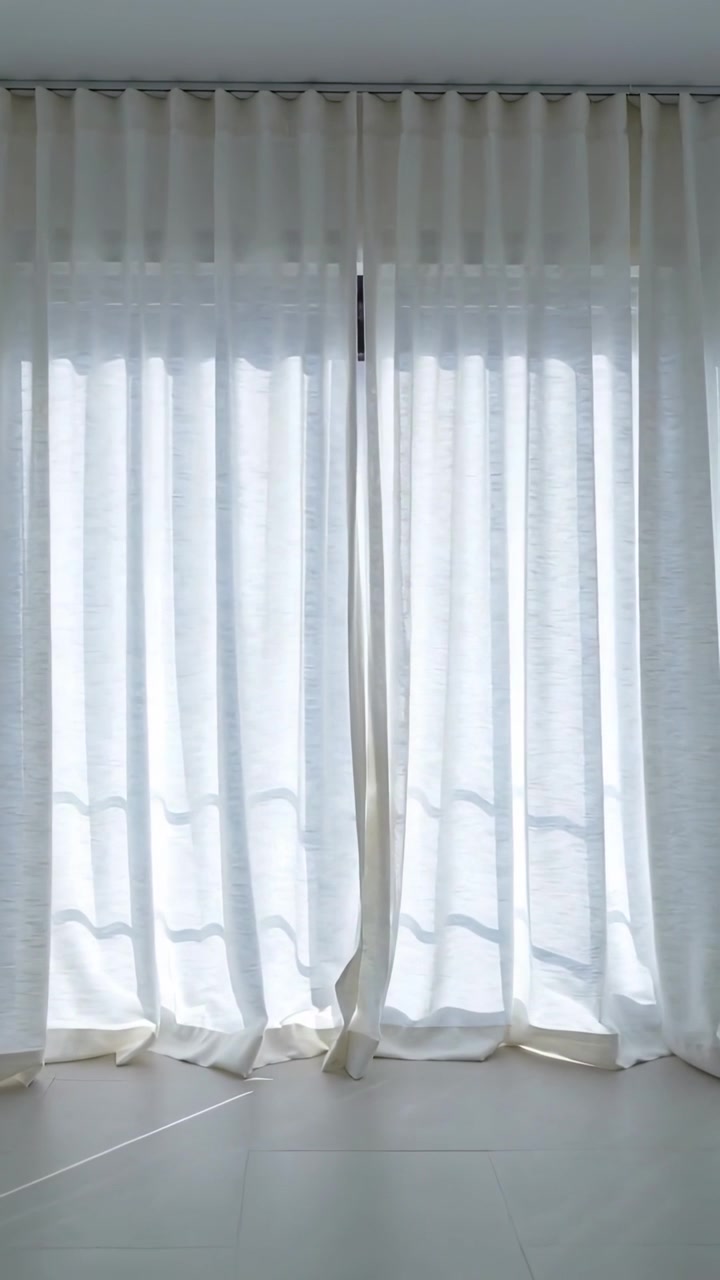 Vídeo vertical: Painéis de cortina pálidos esvoaçando, torcendo e levantando a costura em um quarto claro com a brisa.