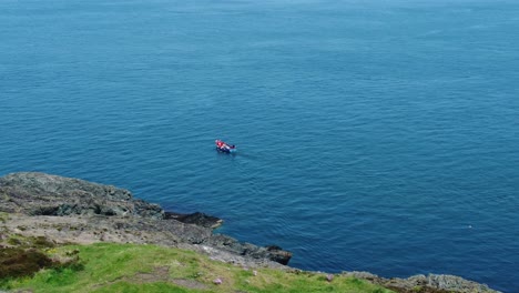 small fishing boat sailing colourful blue ocean water view from welsh hillside slope