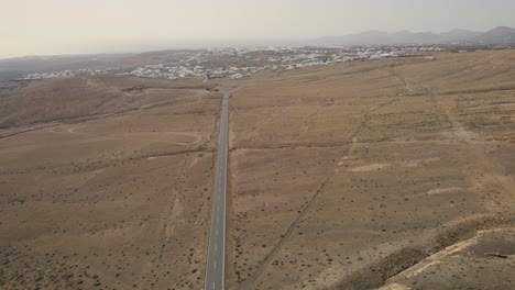 Vuelo-De-Drones-Sobre-La-Carretera-Que-Conduce-A-Través-Del-Paisaje-De-La-Isla-Volcánica,-Lanzarote,-Islas-Canarias