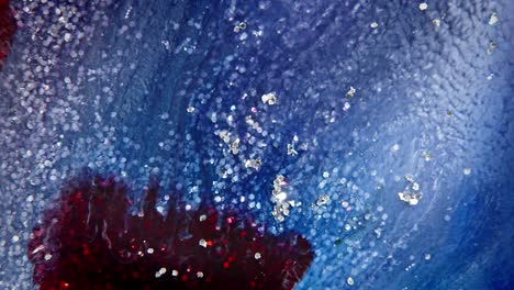 tinta azul y roja dispersándose en el agua con partículas brillantes, creando un fondo abstracto y celestial