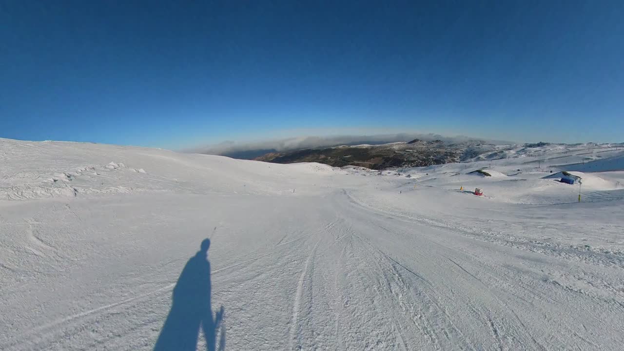 4K action camera POV skiing on a wide, intermediate blue-level slope in Sierra Nevada, Granada, Spain, showcasing a smooth, controlled descent under a pristine blue sky