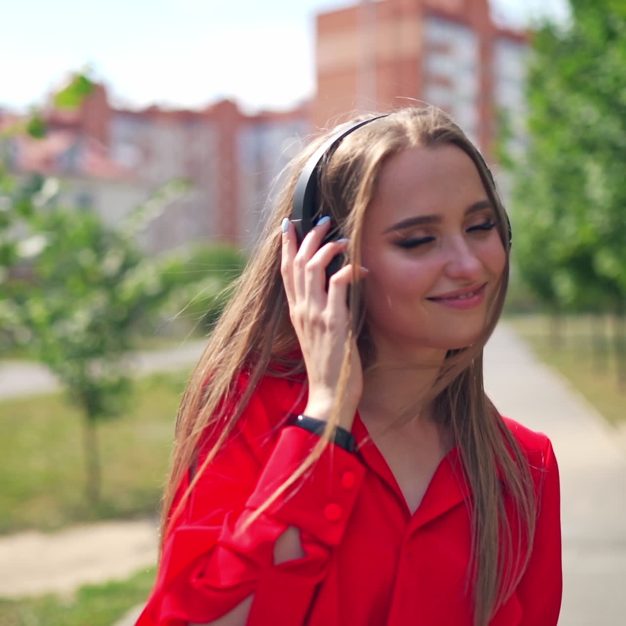 Lovely girl outdoors. Portrait of a young woman with headphones. Beautiful female listening to music in headphones on the city skyscrapers background.