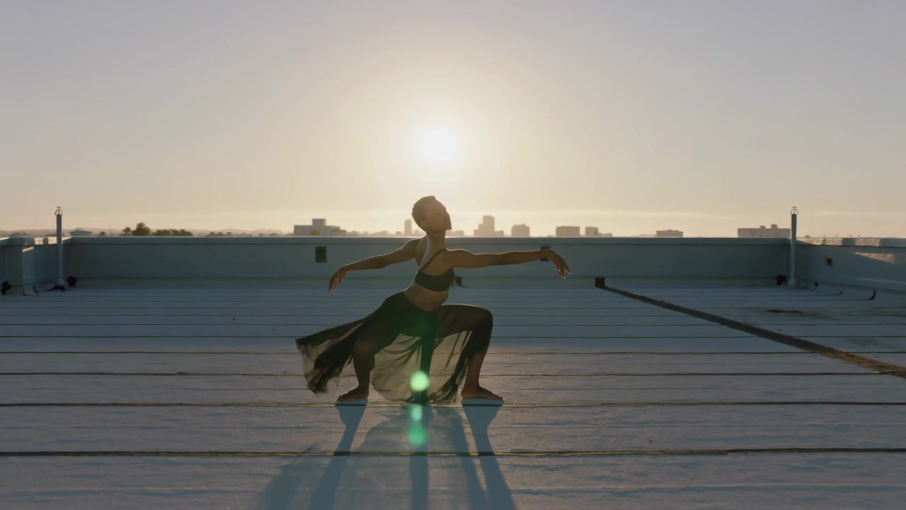 Reagerend op de lage zon, voert een danser een lunge-naar-pointe uit op een dakterras, in danskleding met naden en ventilatieopeningen