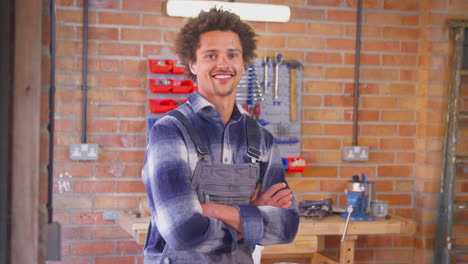 portrait of smiling man wearing overalls in garage workshop at home