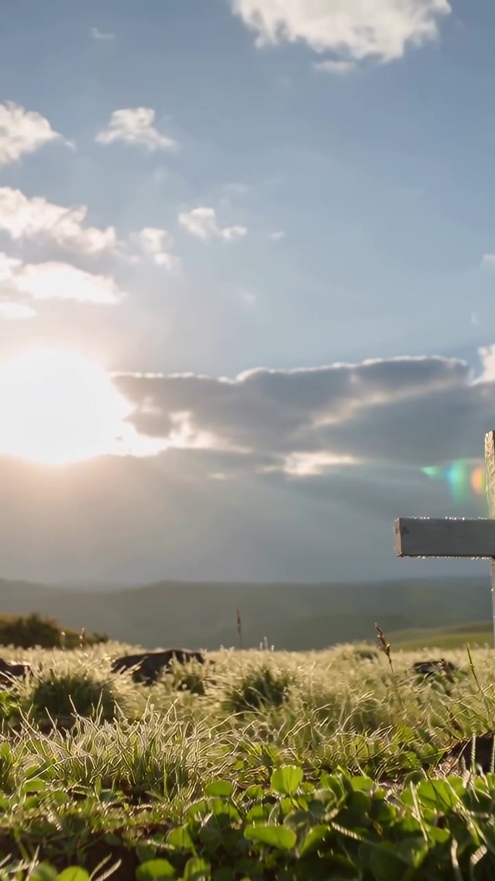 Video verticale: Raggi di sole che illuminano una croce di legno bianca su una collina mentre le nuvole si diradano, spazio per il testo.