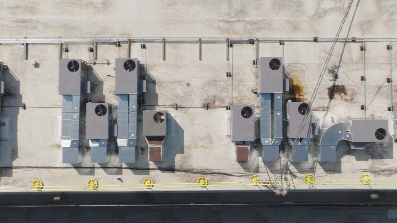 Overhead drone shot of multiple large HVAC units installed on a flat industrial rooftop, showing detailed ventilation systems and piping infrastructure.