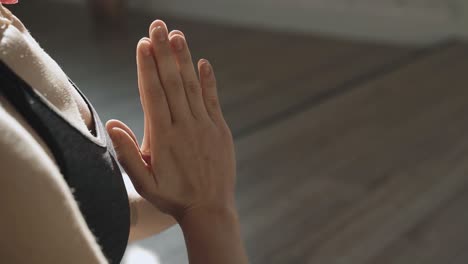 Closeup-shot-of-relaxed-young-woman-in-sportswear-who-is-meditating-indoors-in-lotus-position-sitting-at-home-enjoying-meditation-with-hands-in-namaste