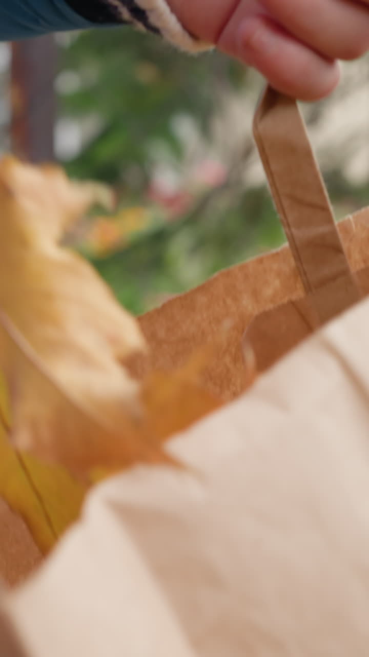 primer plano de un niño colocando suavemente una hoja seca de otoño en una bolsa de papel marrón, mostrando una actividad ecológica y una conexión con la naturaleza colorida en un fondo borroso