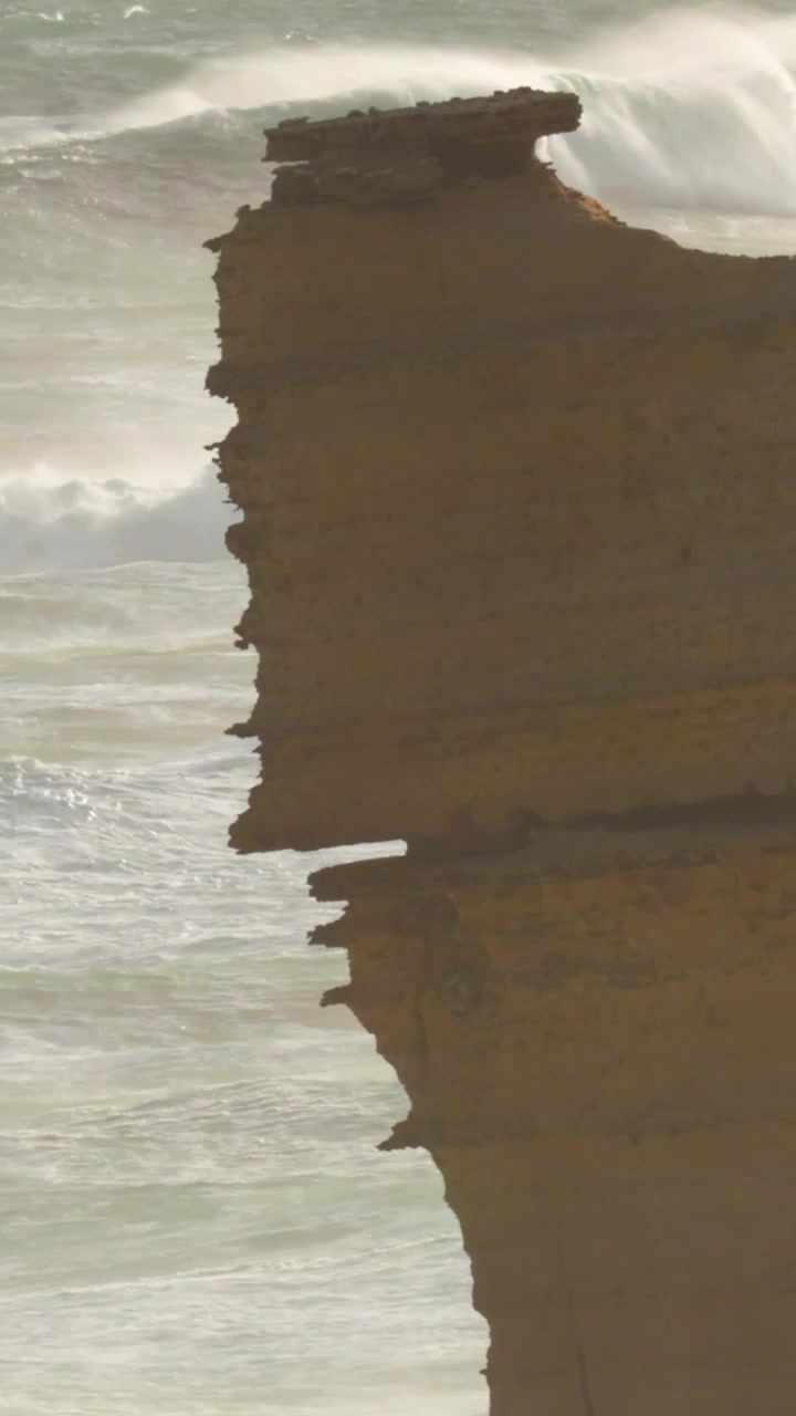 Una vista serena di onde che si infrangono contro una formazione rocciosa sulla Great Ocean Road, catturata con luce naturale.