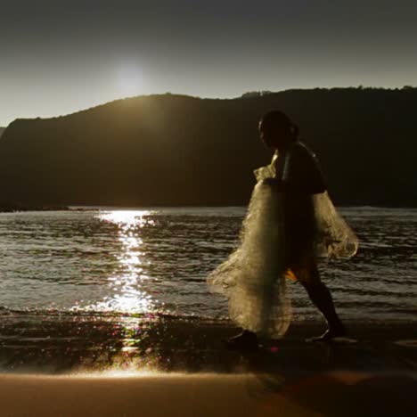 a gorgeous shot as a fisherman walks in front of the sunset with his net in slow motion 1