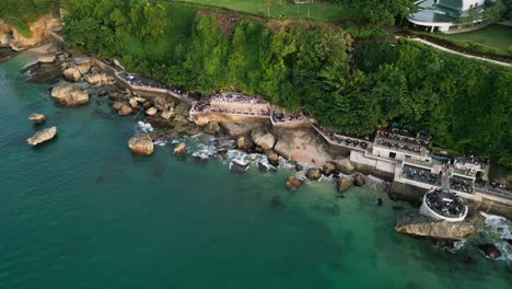 guests enjoy dinner at a bali bar built on a natural rock formation surrounded by the sound of waves and views of the clear blue ocean creating a peaceful and unforgettable dining scene