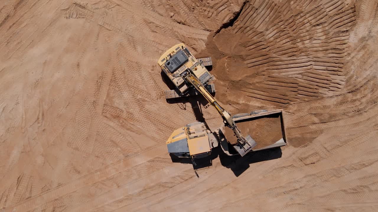 Excavator loading sand into large truck, aerial view