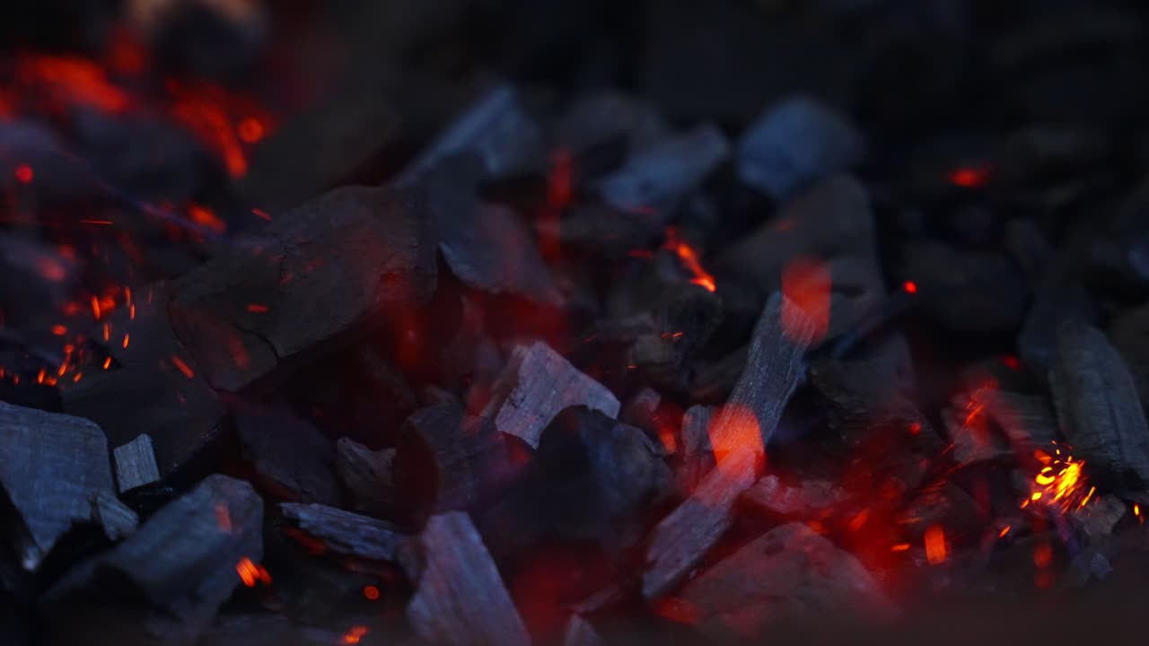 Burning charcoal pieces with bright orange flame, dark blurred background, slow motion
